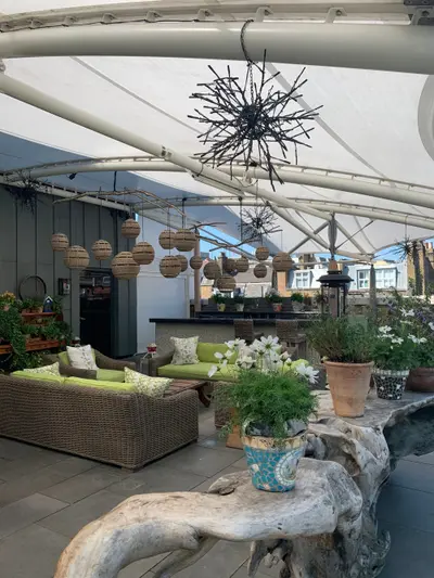 The roof terrace at Ham Yard Hotel, wicker seating and planters under a canopy above the Soho rooftops
